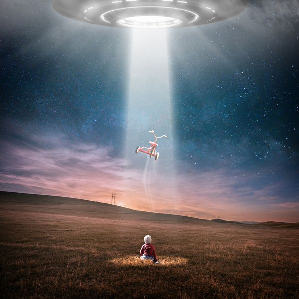 A UFO shining a beam on a child in a field and pulling up the child's tricycle.