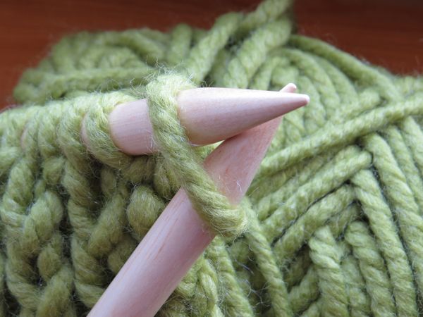 Knitting needles crossing at their tips and green wool.