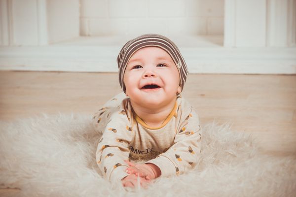 A baby lying stomach-down on a sheepskin rug and smiling.