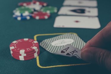 Poker chips and cards on a poker table. Fingers are lifting up the corner of two cards.