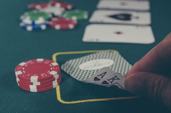 Poker chips and cards on a poker table. Fingers are lifting up the corner of two cards.