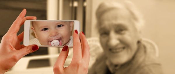 A woman's hands hold a phone that is pointing at an elderly lady. However, the viewfinder shows a baby.