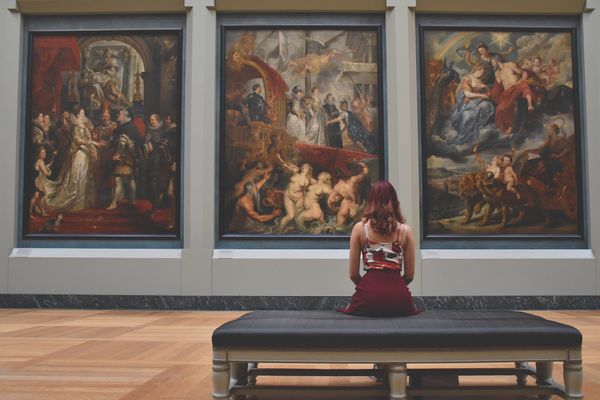A girl sitting on a bench and looking at large paintings in a gallery.