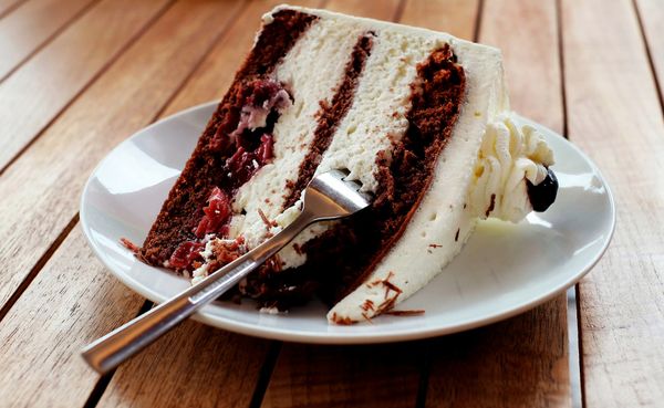 A red and white piece of cake on a plate. There is a fork in the cake.