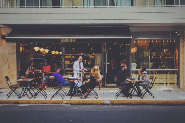 People seated outdoors at a restaurant. A waiter is talking to them.