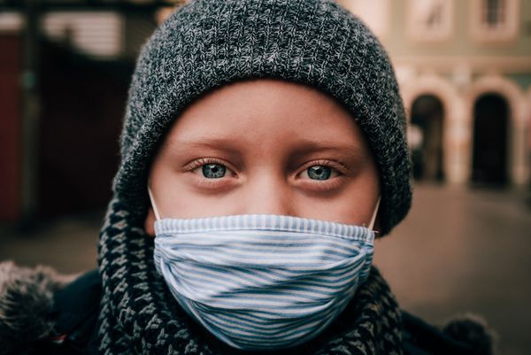 A blue-eyed child wearing a woolen hat, scarf, and face mask.