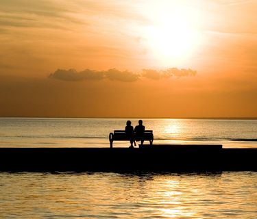 A couple sitting on a bench watching the sun go down.