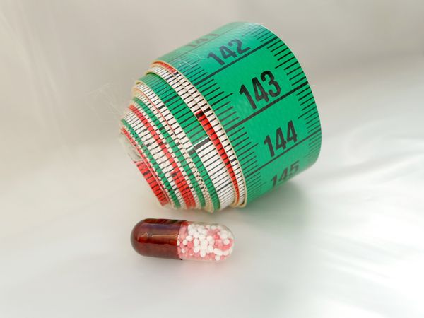 A rolled-up measuring tape next to a pill.