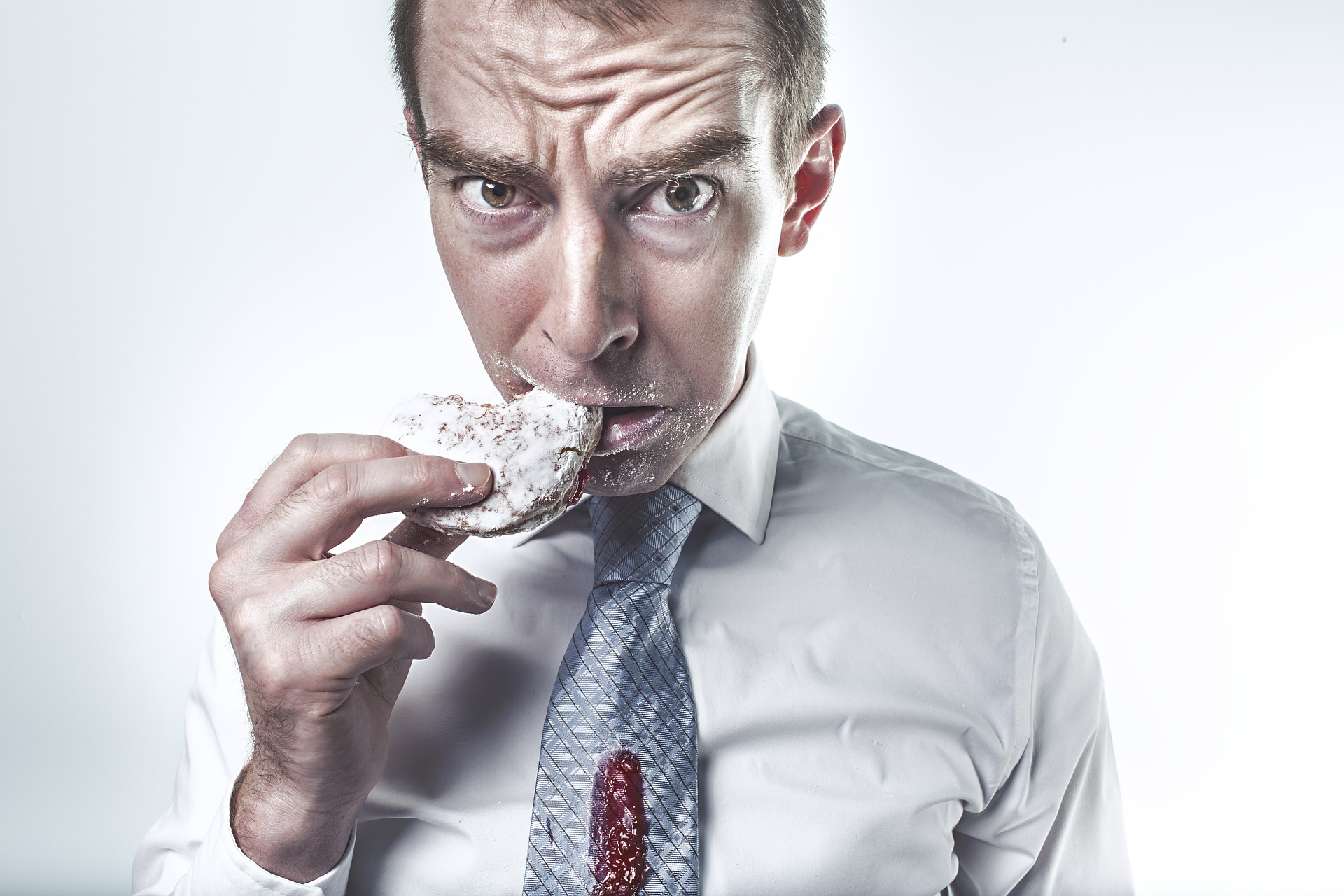 a man with jam on his tie and sugar on his face is biting a donut