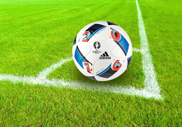 A soccer ball with Euro 2016 and Adidas labeling placed in the corner of a soccer pitch.