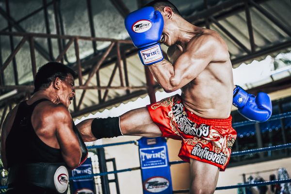 A Muay Thai kickboxer is off the ground and kicking his trainer near his chest.