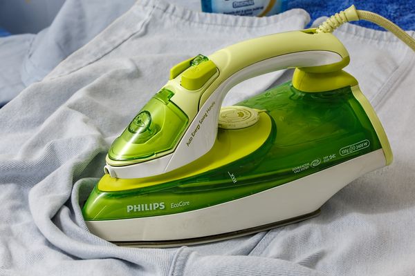 A green Philips iron sitting on a pair of light blue jeans.
