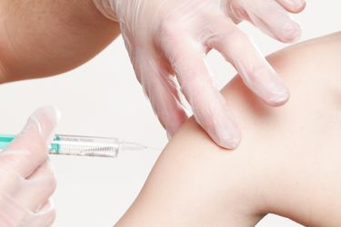 Gloved hands vaccinating a person via needle in their shoulder.
