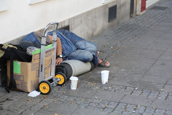 A person sleeping rough on the street next to a cardboard box.