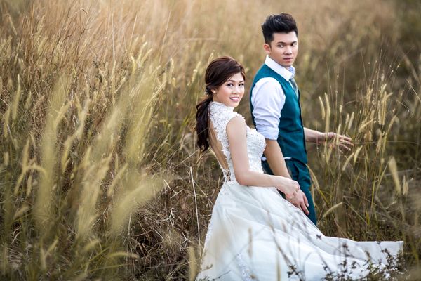 A bride in a white wedding dress and a groom in a green suit are standing with flax bushes all around them.