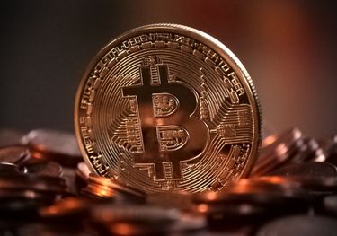 A gold-colored coin with the bitcoin symbol and words like 'peer to peer.' It sits on a pile of coins.