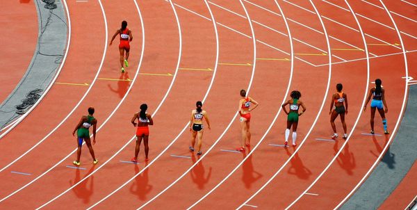 Runners lined up to race on a running track and one runner has gone ahead in false start.