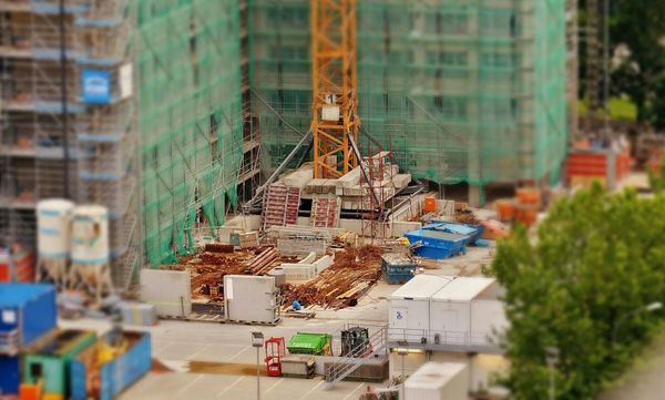 A building construction site with the base of a crane and piles of materials in the center. The picture is blurred at the edges.