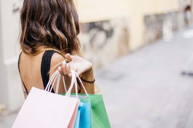 The back of a woman with shopping bags in her hand which she is holding up next to her shoulder.