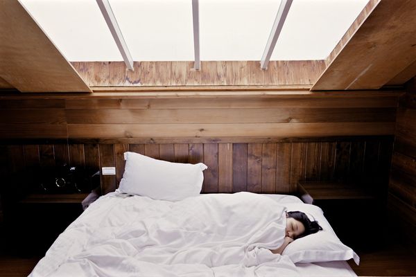 A woman sleeping in bed in a wooden cabin under a bright skylight.