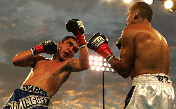 Two shirtless boxers are facing off. There is a stadium light in the background.