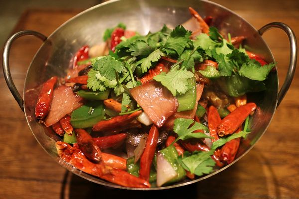 A dish with pork, peppers and cilantro, in a wok.