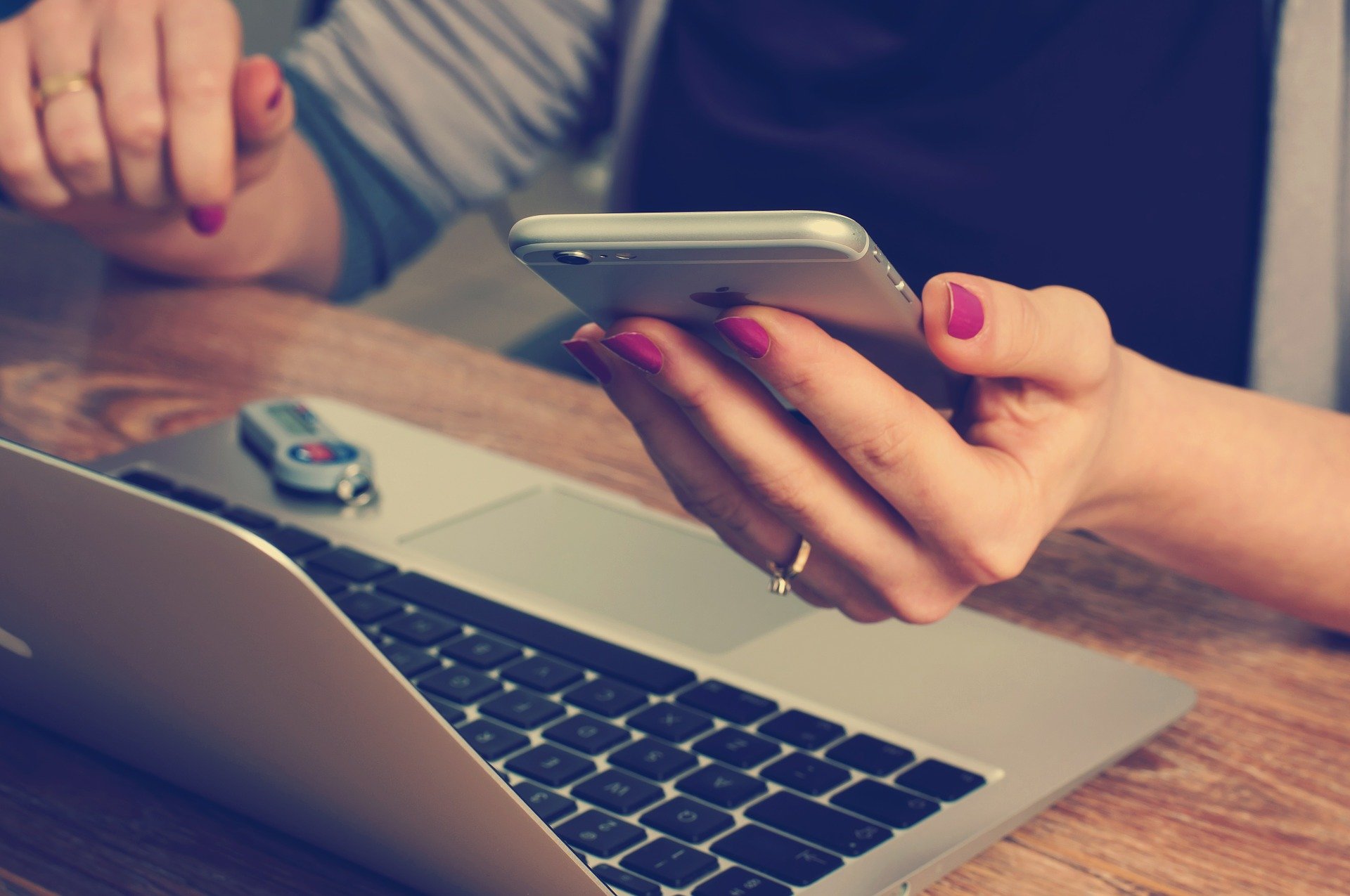 a woman holding a smartphone next to a notebook computer