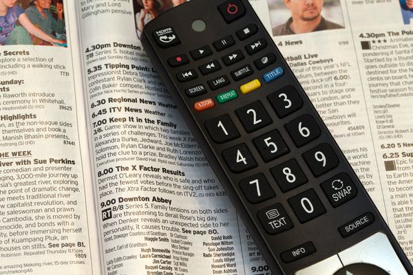 A TV remote control on an open TV guide magazine.