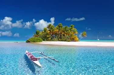 A tropical island with white sand, palm trees, and clear blue water.