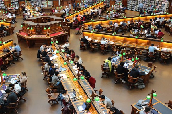 A university library filled with students studying on long tables.