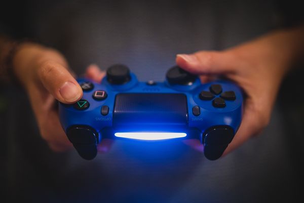 Hands on a blue PlayStation controller which has a glowing light.