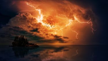 Lightning and storm clouds over an island in the ocean.