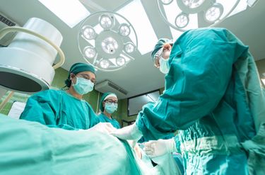Surgeons and nurses performing surgery around an operating table.