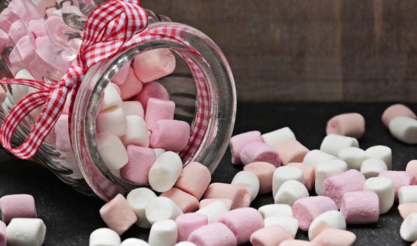 A jar of pink and white marshmallows on its side and spilling out.